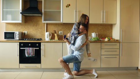 Young man making proposal to his girlfriend in the kitchen at homeの写真素材