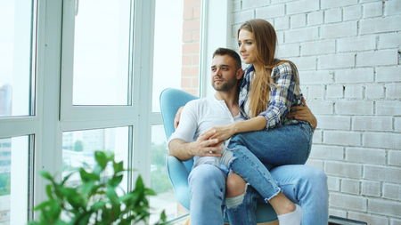 Beautiful young couple relax sitting on chair and enjoying view from balcony of new loft apartmentの写真素材
