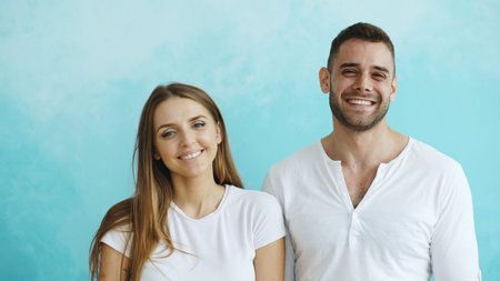 Portrait of young happy couple smiling and laughing into camera on blue backgroundの写真素材