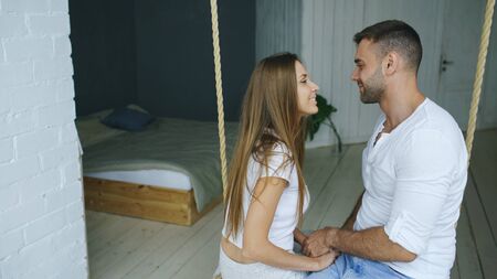 Happy loving couple sitting in swing in bedroom at homeの写真素材