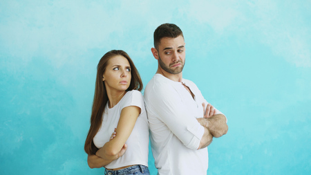 Young couple upset and angry each other standing rear on blue backgroundの写真素材