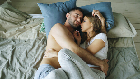 Young beautiful and loving couple kissing on bed in the morningの写真素材