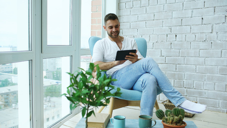 Attractive man using digital tablet sitting in chair at balcony in loft modern apartmentの写真素材