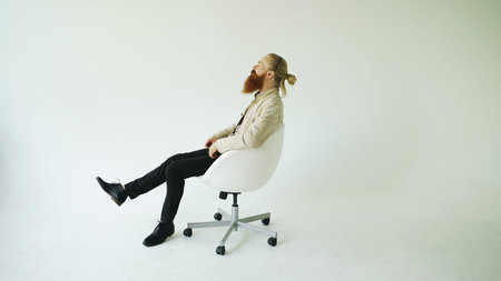 Smiling bearded man turning on swivel office chair on white backgroundの写真素材