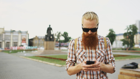 Bearded tourist man with backpack walking street and using smartphone for view map outdoorsの写真素材