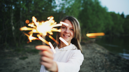 Portrait of young smiling woman with sparkler celebrating at beach partyの写真素材