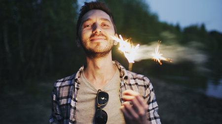 Portrait of young smiling man with sparkler celebrating at beach partyの写真素材