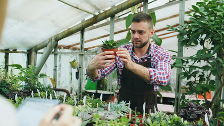 Young man working in garden center. Attractive guy check and count flowers using tablet computer during work in greenhouseの写真素材