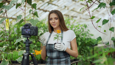 Young smiling blogger woman florist in apron talking and recording video blog for her online vlog about gardeningの写真素材