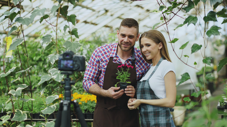 Young smiling blogger couple gardeners in apron holding flower talking and recording video blog for online vlog about gardeningの写真素材