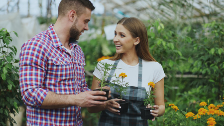 Young friendly woman florist talking to customer and giving him advice while working in garden centerの写真素材