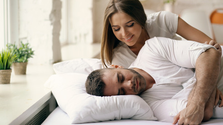Young beautiful and loving couple wake up at the morning. Attractive woman kiss and hug his husband in bedの写真素材