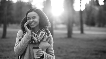 Attractive mixed race girl talking smartphone and drinking coffee in city park with bags. Young woman after shopping on mall saleの写真素材