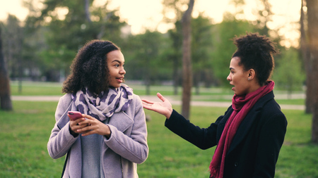 Two attractive mixed race women surpisely have meeting in the park near mall storeの写真素材