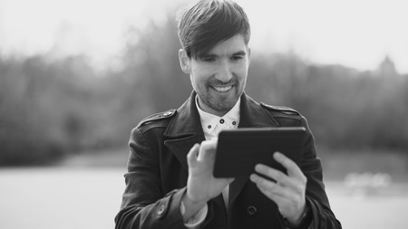 Young smiling businessman using tablet computer during break at the streetの写真素材