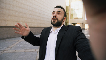 Young bearded businessman talking smartphone having online video chat business meeting outdoorsの写真素材