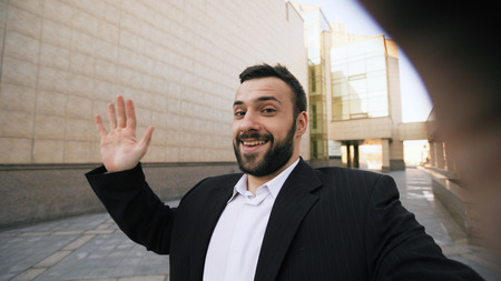 Young bearded businessman talking smartphone having online video chat business meeting outdoorsの写真素材