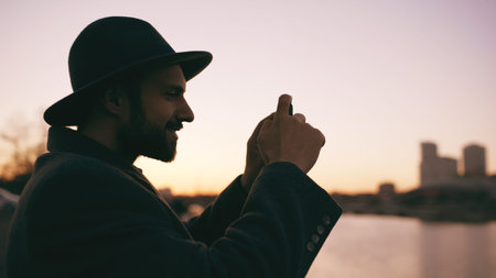 Silhouette of traveler man in hat taking panoramic photo of the city skyline on his smartphone...