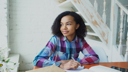 Teenage curly haired mixed race young girl sitting at the table concentrating focused learning lessons for examination to univercityの写真素材