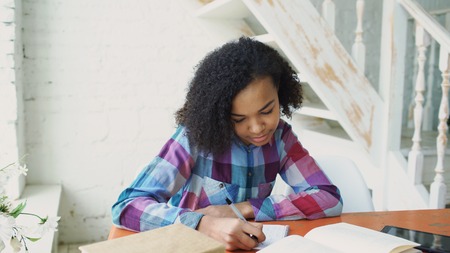 Teenage curly haired mixed race young girl sitting at the table concentrating focused learning lessons for examination to univercityの写真素材