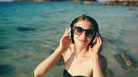 Happy beautiful woman listening to music on wireless headphones on beach near seaの写真素材