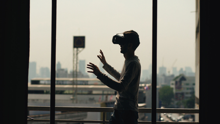 Silhouette of young man watching movie in VR headset and have virtual reality experience on hotel room balconyの写真素材