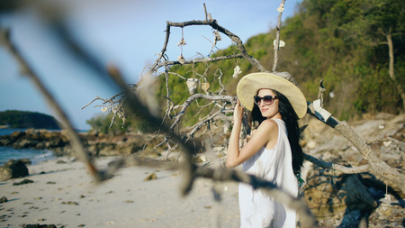 Young sexy woman in sunglasses and hat smiling and posing near tree at beautiful tropical beachの写真素材