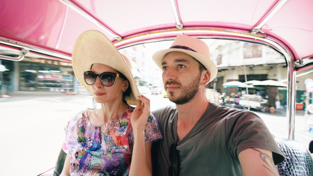 Young handsome man in hat with his girlfriend ride on traditional thai bus songteo. Couple travel Thailand during their honeymoonの写真素材