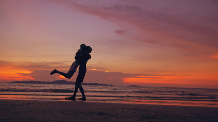 Silhouette of happy loving couple meet and play at the beach on sunset in ocean shoreの写真素材