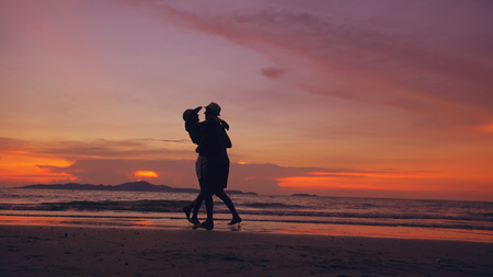 Silhouette of happy loving couple meet and play at the beach on sunset in ocean shoreの写真素材