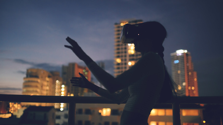Young woman on rooftop terrace using virtual reality headset and having VR experience at nightの写真素材