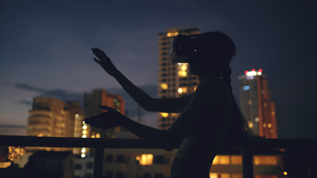 Young woman on rooftop terrace using virtual reality headset and having VR experience at nightの写真素材