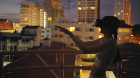 Young woman on rooftop terrace using virtual reality headset and having VR experience at nightの写真素材