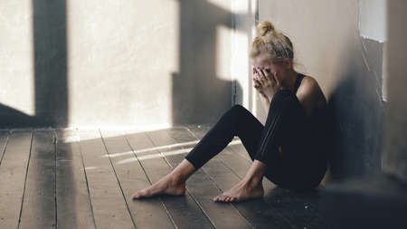 Closeup of young teenage girl dancer crying after loss perfomance sits on floor in hall indoorsの写真素材