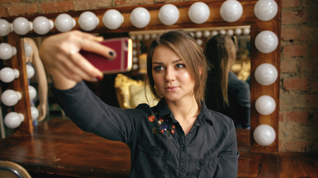 Beautiful young woman making selfie portrait on a smartphone in dressing room indoorsの写真素材