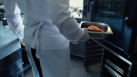 Professional chef man put meat dish into oven at restaurant kitchenの写真素材