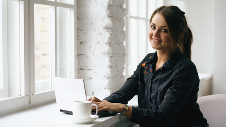 Young smiling student woman sit in coffee shop at table with laptop indoorsの写真素材