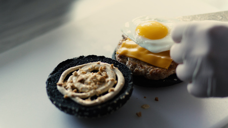 Closeup of chef cook grilled black burgerwith sauce and eggs on kitchen boardの写真素材