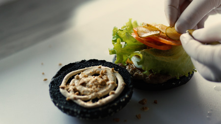 Closeup of chef cook grilled black burgerwith sauce and vegetables on kitchen boardの写真素材