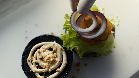 Closeup of chef cook grilled black burgerwith sauce and vegetables on kitchen boardの写真素材