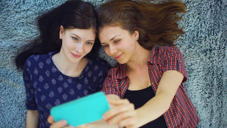Top view of two pretty girls in pajamas making selfie portrait on bed in bedroom at homeの写真素材