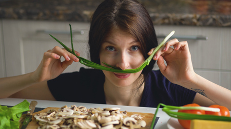 beautiful funny woman cook play with green onion on table in kitchen at homeの写真素材