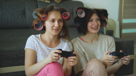 Two funny women play console games with gamepad and have fun at homeの写真素材