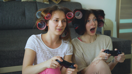 Two funny women play console games with gamepad and have fun at homeの写真素材