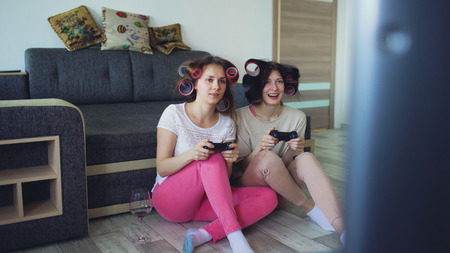 Two funny women play console games with gamepad and have fun at homeの写真素材