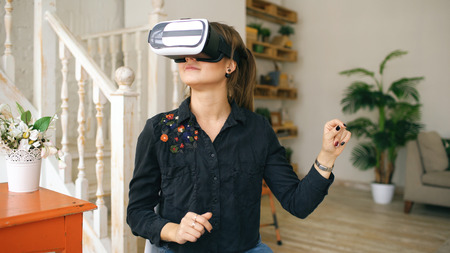 Woman in VR headset looking up and trying to touch objects in virtual reality at home indoorsの写真素材