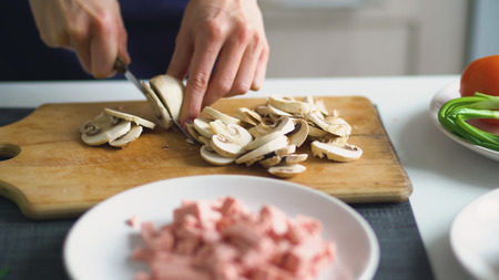 Closeup of girl hands cutting the mushrooms on wooden board for pizza in the kitchen at homeの写真素材