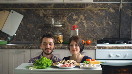 beautiful smiling couple above the table with vegetables while cooking in kitchenの写真素材