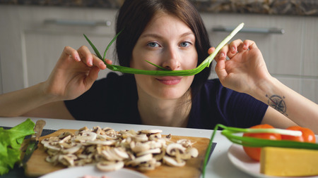 beautiful funny woman cook play with green onion on table in kitchen at homeの写真素材