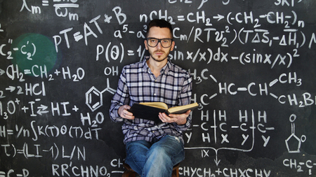 Young scientist man read book in chemical and mathematical equations wall room interiorの写真素材